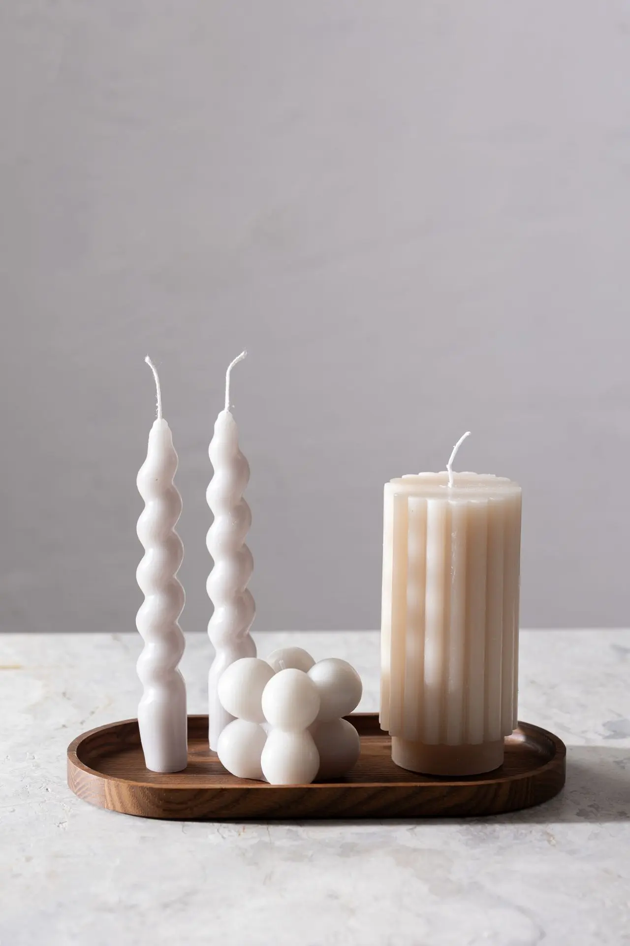 Owalna drewniana taca na świece z czterema ozdobnymi, białymi świecami na marmurowym blacie. Idealna jako taca dekoracyjna na świece do salonu,An oval wooden candle tray with four decorative white candles on a marble top. Perfect as a decorative candle tray for the living room