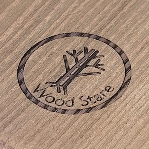Okrągłe logo Wood Stare wypalone w ciemniejszym drewnie – grawery na drewnie o wysokim kontraście, Round Wood Stare logo burned into darker wood – high-contrast wood engravings
