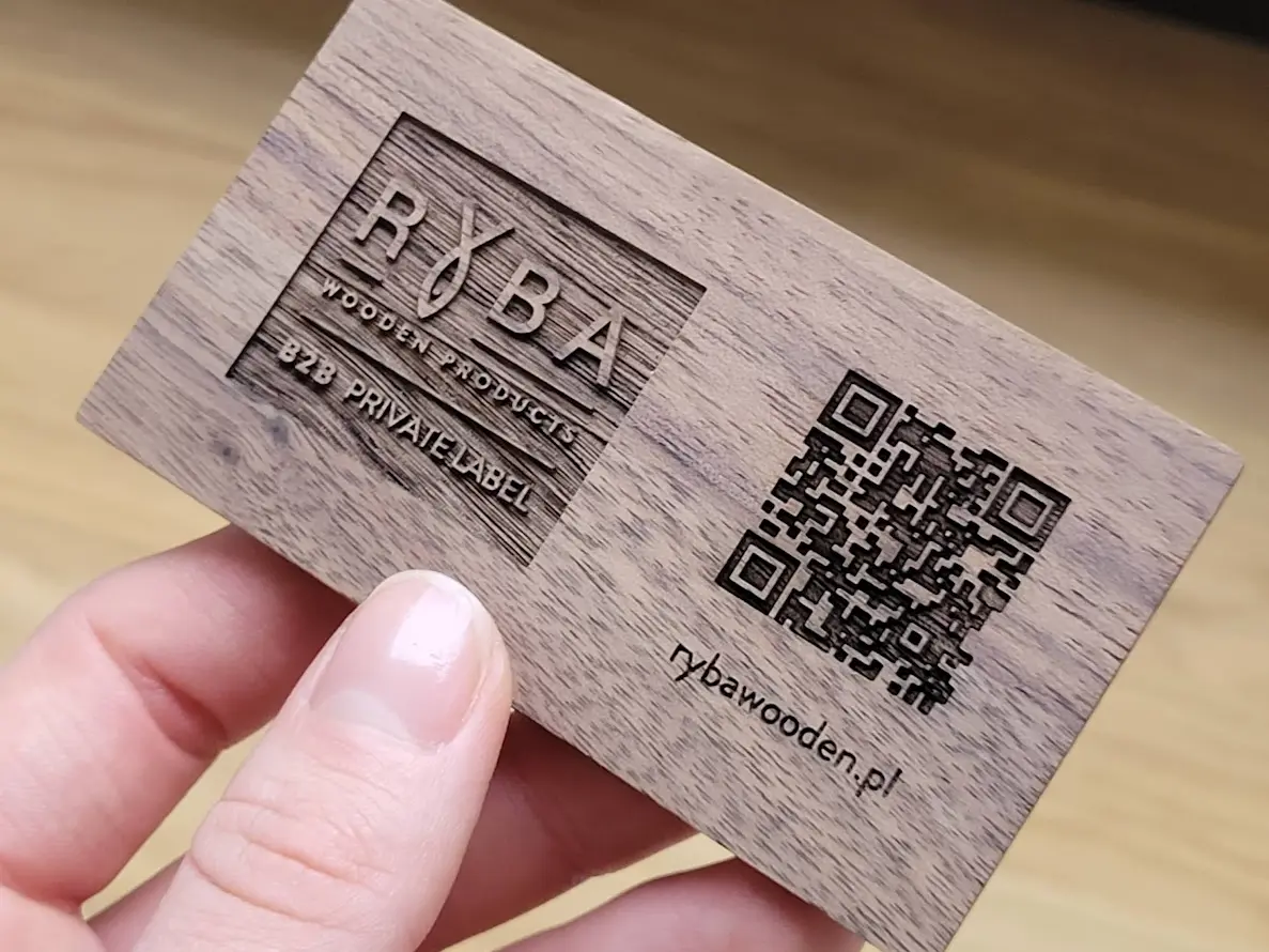 Drewniana wizytówka z grawerem RYBA WOODEN PRODUCTS i kodem QR to przykład precyzyjnego grawerowania laserowego w drewnie przez polskiego producenta, A wooden business card engraved with RYBA WOODEN PRODUCTS and a QR code is an example of precise laser engraving on wood by a Polish manufacturer 