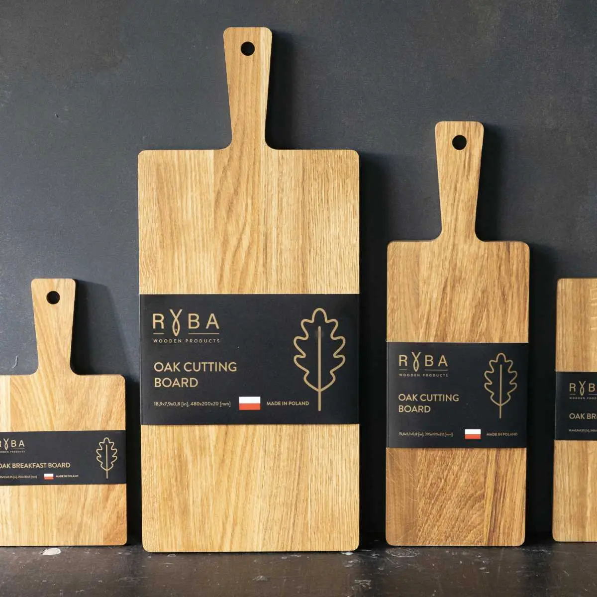 Dębowe deski do krojenia w różnych rozmiarach – każda deska z rączką posiada elegancką czarną papierową banderolę z logo Ryba Wooden Products,Oak cutting boards in various sizes – each board with a handle features an elegant black band with the Ryba Wooden Products logo