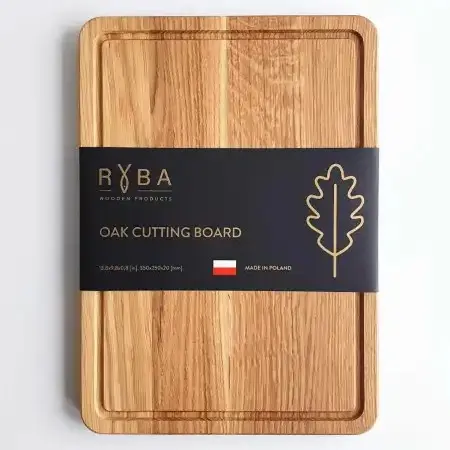 Prostokątna deska do krojenia z drewna z wyfrezowanym rowkiem, na którą nałożona jest szeroka papierowa opaska z informacjami o produkcie wyprodukowanym w PolsceA rectangular wooden cutting board with a groove, wrapped in a wide paper band bearing information about the product, which is manufactured in Poland