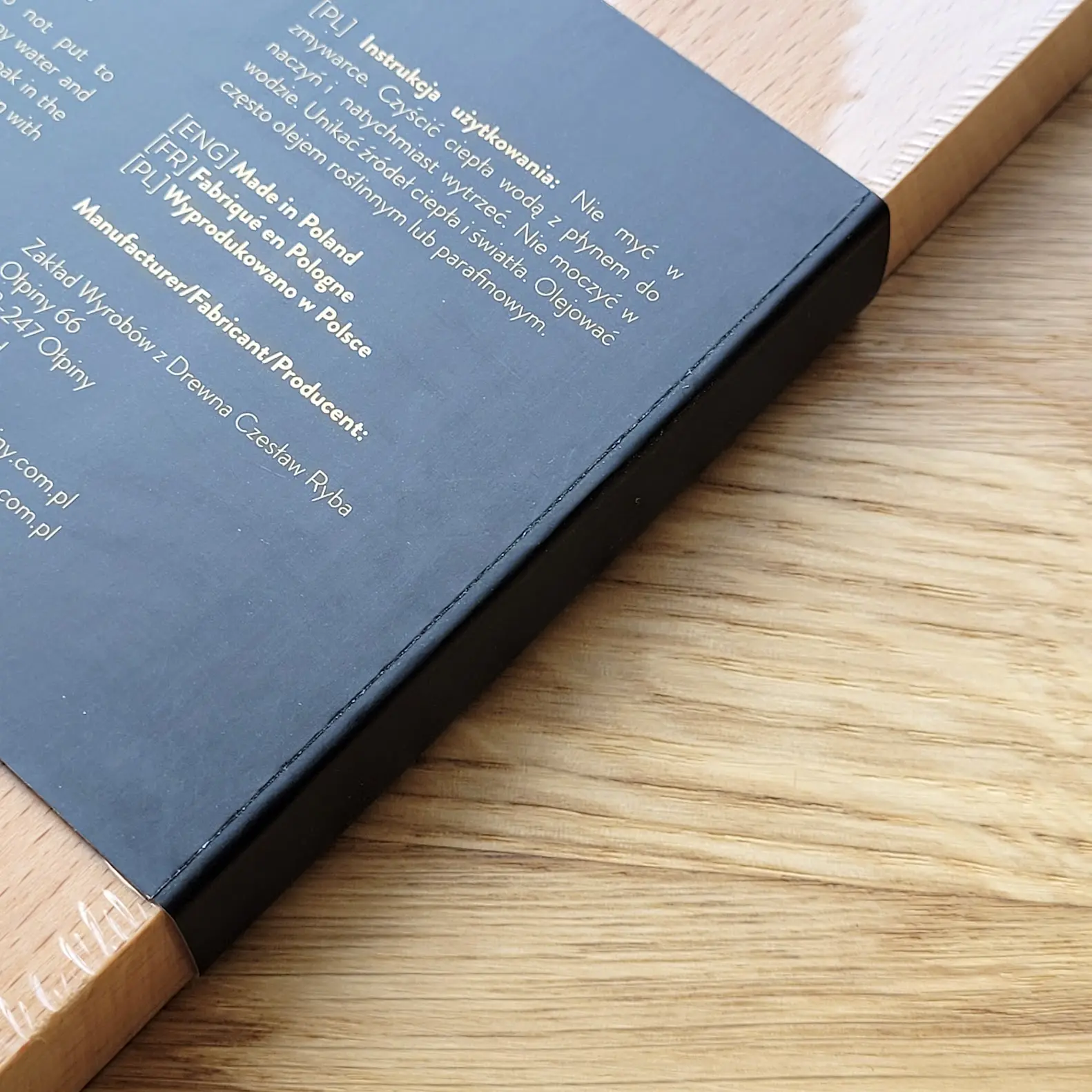 Zbliżenie na wykończenie krawędzi deski – folia ochronna ściśle przylega do drewna, zabezpieczając grawer i powierzchnię,Close-up of the board edge finish – the protective foil adheres tightly to the wood, protecting the engraving and surface